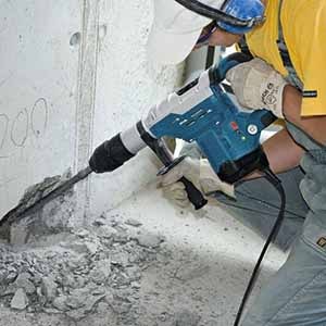 Trabalhador utilizando um martelete rompedor em uma parede de concreto.