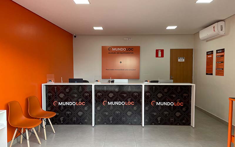 Interior da loja MundoLoc, com 3 bancadas para atendimento, ar-condicionado, mesa de testes, água, café e cadeiras para atendimento.